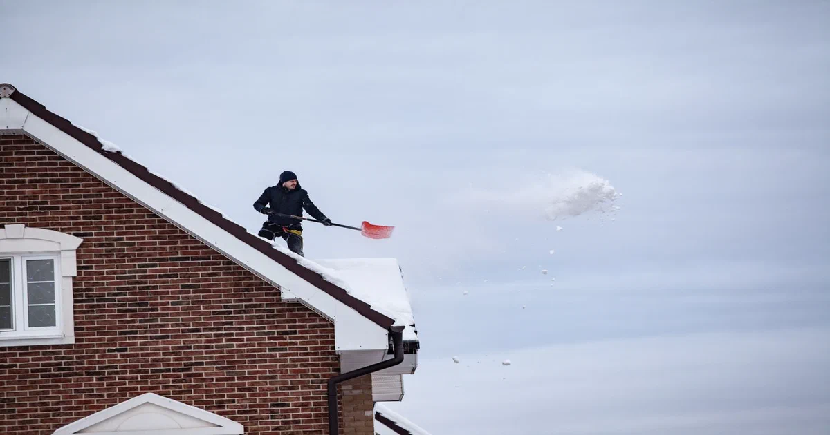 Déneigeur retirant la neige du toit en pente d'une maison de brique avec une pelle